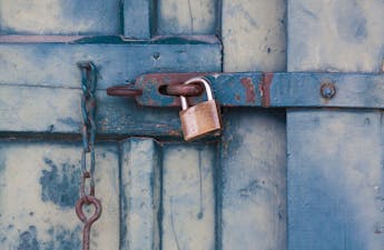 A close-up of a rusty padlock securing a blue painted wooden door with chain and bolt.
